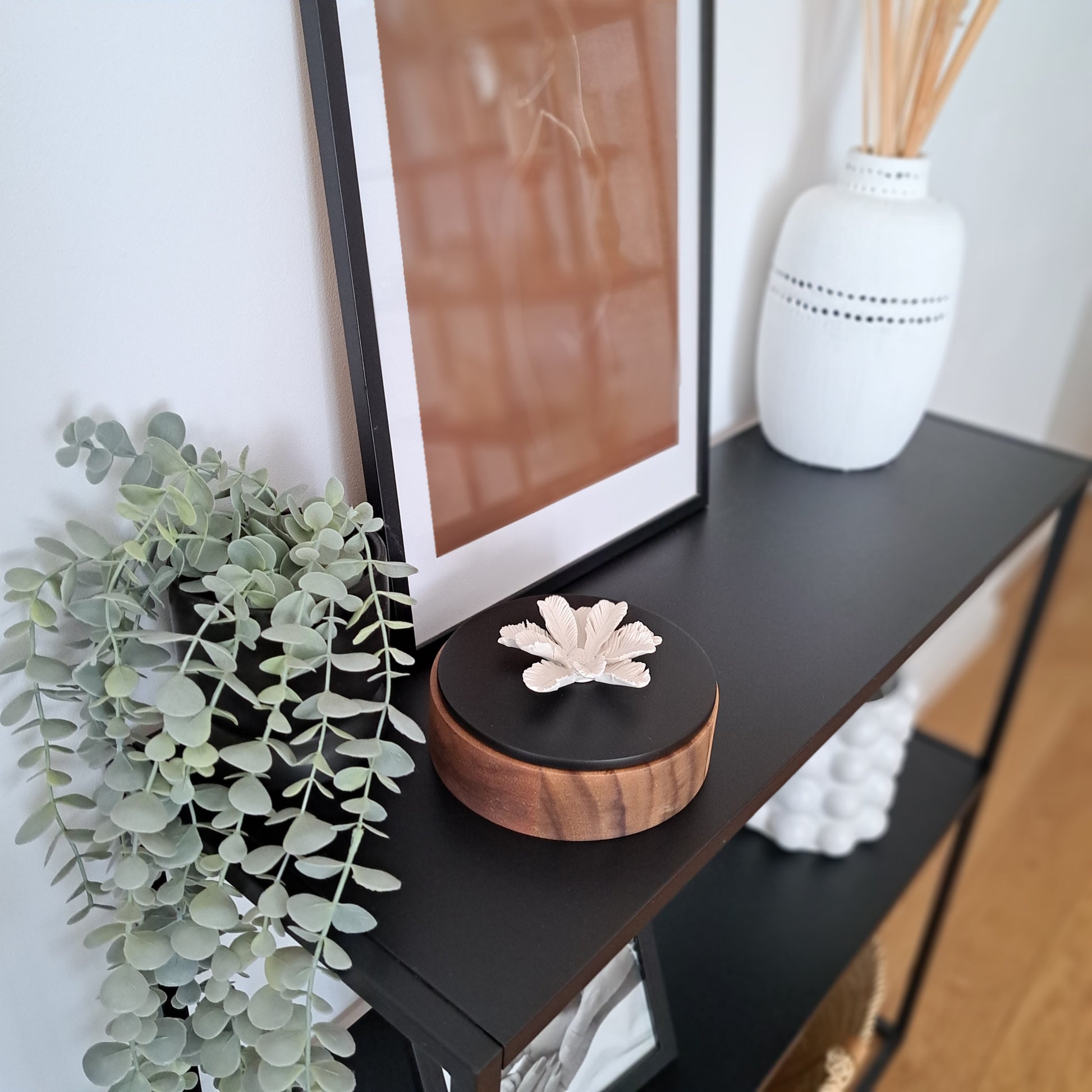 Coffret en bois et son couvercle noir.  La fleur de palmier en porcelaine blanche sur le dessus, apporte de la délicatesse à cet boite qui allie utilité, beauté et senteur agréable. Et oui, quelques gouttes de parfum ou d'huile essentielle au cœur de la fleur transformeront ce coffret en diffuseur de senteurs. Le cadeau parfait pour la fête de mères